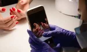 Ręce w fioletowych rękawiczkach robią zdjęcie pięknych, czerwonych paznokci na telefonie. Oto jak zrobic ladne zdjecia paznokci.