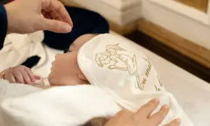Dziecko otulone w biały kocyk z aniołkiem, przygotowywane do chrztu. To ważny moment, który potwierdzi zaświadczenie od księdza do chrztu.