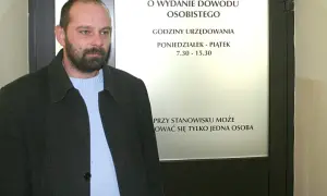 Mężczyzna czeka na informację, ile kosztuje wyrobienie dowodu osobistego. Tablica informuje o godzinach urzędowania.