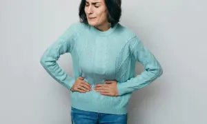 Kvinna med händerna på magen, ansiktet förvridet av smärta. Ett tydligt tecken på stressmage symptom.