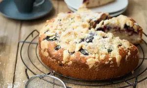 Ein saftiger, schneller Brombeerkuchen mit Streuseln, der auf einem Gitterrost abkühlt. Daneben eine Kaffeetasse und ein Stück Kuchen.