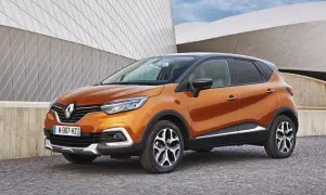Pomarańczowy Renault Captur 2016 z czarnym dachem zaparkowany na brukowanej nawierzchni przed nowoczesnym budynkiem.