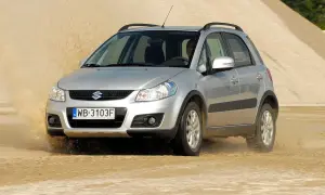 Srebrny Suzuki SX4 pokonuje piaszczystą wydmę, wzbijając tumany kurzu.