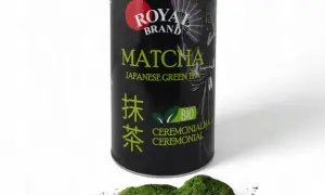 Czarna puszka z zieloną herbatą matcha Royal Brand i garść proszku matcha na białym tle.