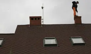 Mężczyzna w pomarańczowych spodniach stoi na kominie i czyści go szczotką.