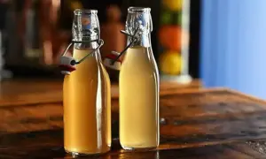 Dwie butelki z zamknięciem pałąkowym, wypełnione złotym płynem, być może domowym sokiem z brzoskwini (peachtree).