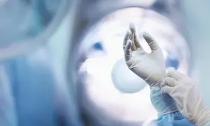 Chirurg zakłada rękawiczki. Wiele osób zastanawia się, jakie są najbardziej opłacalne zawody, a ten zawód z pewnością do nich należy.