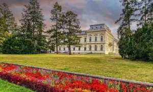 Piękny budynek sanatorium otoczony drzewami i kolorowymi kwiatami. Dowiedz się o nowe zasady wyjazdu do sanatorium na NFZ.