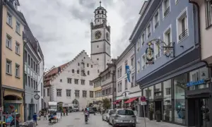 Der Blaserturm Ravensburg ragt über eine belebte Gasse mit Geschäften und Menschen.