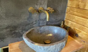 Lavabo in pietra grezza, rubinetteria in ottone e rivestimento in legno: perfette idee bagno montagna per un'atmosfera rustica e accogliente.