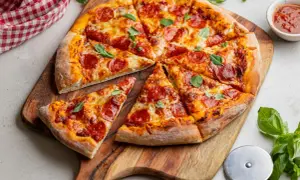 Apetyczna pizza pepperoni z ciągnącym serem i świeżą bazylią na drewnianej desce.
