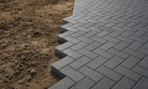 Posa di autobloccanti per esterno in grigio, con un motivo a spina di pesce, che si estendono su un terreno sabbioso.