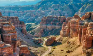 Beeindruckende Schluchten und Berge prägen die Kasachstan Landschaft. Ein gewundener Weg führt durch das Tal, umgeben von roten Felsformationen und grünen Hängen.