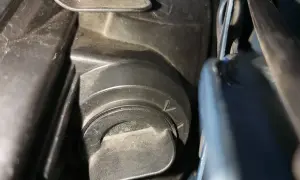 Opel Meriva B wymiana żarówki mijania. Widoczny element mocowania osłony reflektora, przygotowanie do wymiany.