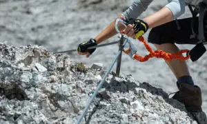 Ręce w rękawiczkach pewnie trzymają linę na via ferrata Słowacja. Pomarańczowa lonża z karabinkami zapewnia bezpieczeństwo.