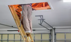 Osoba na drabinie przy wyłazie strychowym. Dowiedz się, jak uszczelnić wyłaz strychowy, by oszczędzać energię.