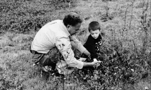 Uomo e bambino in ginocchio tra l'erba, intenti a raccogliere qualcosa. Un momento di condivisione nella natura.
