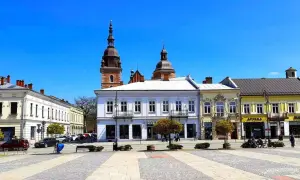 Słoneczny rynek w Nowym Sączu z zabytkowymi kamienicami i wieżą kościelną w tle.