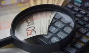 Lupe über 50-Euro-Scheinen auf einem Taschenrechner. Analyse von Betriebskosten und Umlageausfallwagnis.