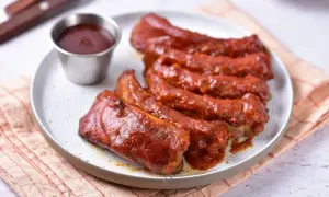 Soczyste żeberka w sosie BBQ, podane na talerzu z małą miseczką sosu. Idealne na letniego grilla.