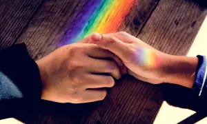 Dłonie splecione na drewnianym blacie, na których widać tęczowe refleksy. To jak pierścionek nastroju znaczenie kolorów, symbolizujący różnorodność i nadzieję.