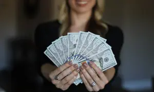 Kobieta trzyma wachlarz banknotów 100-dolarowych. Rozdzielność majątkowa u notariusza to krok do finansowej niezależności.