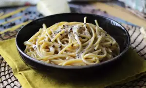 Miseczka spaghetti cacio e pepe, z kremowym sosem serowym i pieprzem, na żółtej serwetce.