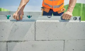 Budowniczy sprawdza poziom ścianki z bloczków. Dokładne wymierzenie ile suporexu na m2 jest kluczowe dla stabilności konstrukcji.