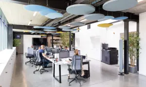 Bureau moderne avec employés concentrés, malgré le bruit ambiant. Des panneaux acoustiques colorés au plafond réduisent le bruit au travail.
