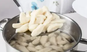 Kopytka gotujące się w garnku, wyjmowane łyżką cedzakową.