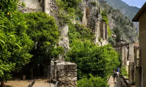 Sentiero tra alberi di agrumi e rovine, con la roccia a picco e la vista sulla limonaia del castel.