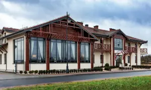 Nowoczesny budynek z drewnianymi elementami architektonicznymi, przypominający początek odyseja ciechocinek. Duże okna, balkony i zadbane otoczenie.