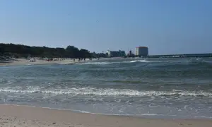 Słoneczny dzień nad Bałtykiem, plaża pełna ludzi, a w oddali widać miasto u ujścia Wieprzy.