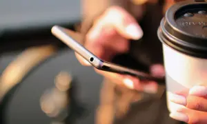Kobieta trzyma telefon i kubek kawy, szukając informacji, jak się doładowuje Play.