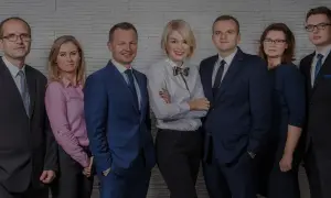 Grupa prawników w eleganckich strojach pozuje do zdjęcia na tle ściany z cegły.