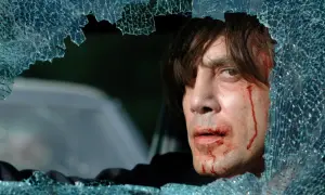 Javier Bardem w jednym z mrocznych filmów, z krwawiącą twarzą, patrzy przez pękniętą szybę.