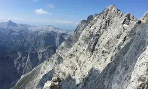 Steile Felsformationen der Watzmann Ostwand im Sonnenschein, mit tiefen Tälern und weiteren Berggipfeln in der Ferne.