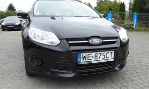 Czarny Ford Focus 2011 z tablicą WE 875CT zaparkowany na kostce brukowej.