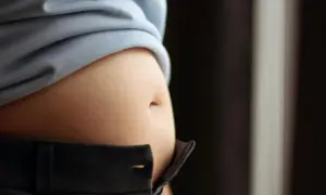 En svullen mage, kanske gravid, syns under en ljusblå tröja och över ett par mörka byxor.