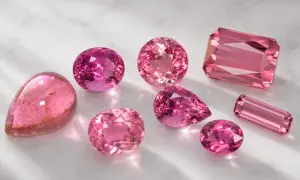 Variedad de turmalina colores rosados, desde el fucsia intenso hasta el rosa pálido, en distintas formas y cortes, brillando sobre una superficie clara.