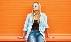 Blondynka w okularach i jeansach, z rozpiętą błękitną koszulą. Idealny przykład, jak nosić koszulę do jeansów na luzie.