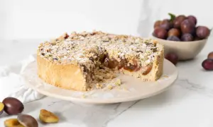 Ein köstlicher Zwetschgenkuchen mit Streuseln, bestäubt mit Puderzucker, steht auf einem Teller. Daneben liegen frische Zwetschgen.