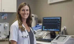 Uśmiechnięta lekarka przy monitorze EKG. Czy nerwica serca wyjdzie na EKG? Zależy od objawów.