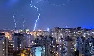 Grzmoty nad miastem, błyskawice rozświetlają nocne niebo. Warto pomyśleć o ubezpieczeniu od przepięć, by chronić swój dom.