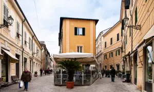 Una donna passeggia nel centro di Senigallia, tra palazzi color pastello e un dehors con palma.