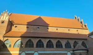 Zamek kapituły warmińskiej w Fromborku, ceglana budowla z pomarańczowym dachem i łukowymi oknami, pod błękitnym niebem.