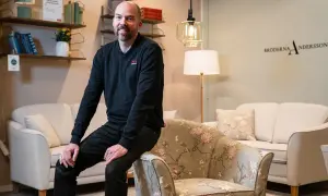 Man sitter på en blommig fåtölj, en Eilersen fåtölj, bredvid en ljus soffa.