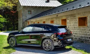La nuova Mercedes GLC 2026 nera lucida parcheggiata davanti a una casa in pietra con tetto grigio, immersa nel verde.
