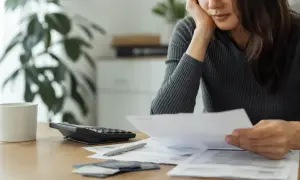 En person sitter vid ett bord med papper, en kalkylator och en kaffekopp. Kanske funderar personen på sitt skuldebrev för bolån.