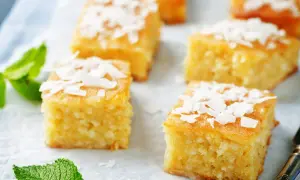 Fette quadrate di torta al cocco, guarnite con scaglie di cocco e foglie di menta fresca.